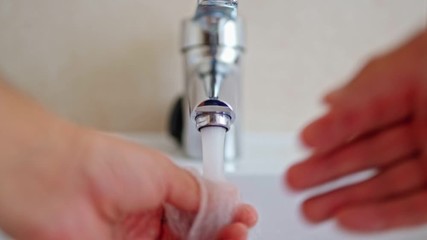 Man is opening tap and filling sink with water close-up. Water running from chrome faucet. Bathroom plumbing. Using water resources.