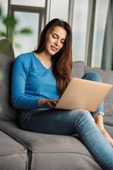Image of happy woman using laptop and smiling while sitting on sofa