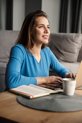 Image of happy woman using laptop and smiling while sitting on floor