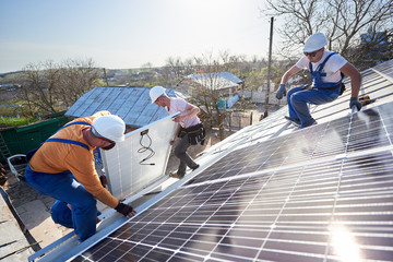 Male team workers installing solar photovoltaic panel system. Electricians lifting blue solar...
