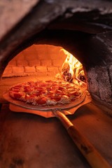 Vertical shot of a delicious cheesy pepperoni pizza inside the brick stone oven