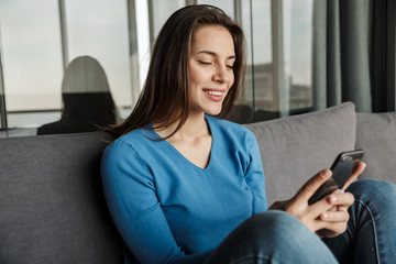 Obraz premium Image of joyful woman using cellphone and smiling while sitting on sofa