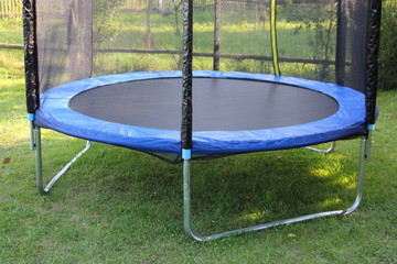Modern empty 8ft trampoline with outside pritection net on green grass on a summer day close-up,...