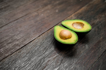 A side view of a ripe avocado halves lying on a wooden background with copy space. One slice with...