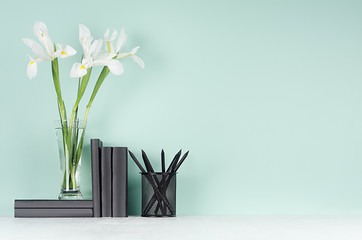 Modern elegant home workplace with black stationery, books, fresh spring white flowers in transparent glass vase green mint menthe interior on white wood table.