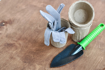 Grey reusable gardening gloves in a peat eco pot for seedlings and a metal shovel next to it on a...
