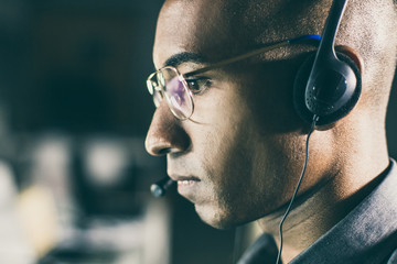 Side view of call center operator. Focused African American man with headset looking at screen....