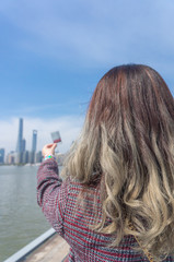 Young asian girl with dyed hair enjoying beautiful China Shanghai cityscape view on the riverside in the sunny day. Raised her hand grabbing a instant photo film of the Shanghai Lujiazui skyscraper