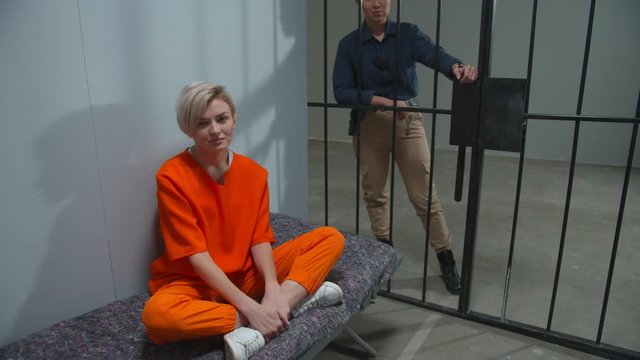 The criminal is sitting in the cell under the supervision of a guard