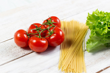 fresh red tomatoes, bunch of spaghetti, green salad leaves on white  wooden table
