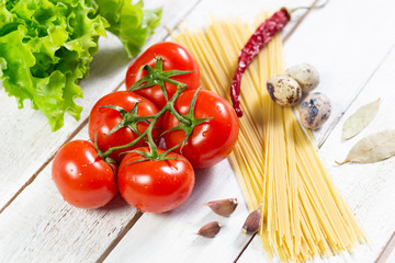 fresh red tomatoes, bunch of spaghetti, green salad leaves, quail eggs, red pepper, garlic, bay leaf on white  wooden table