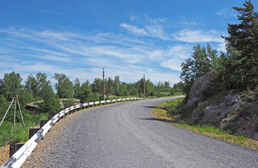 The landscape with the big asphalt road, the low green forest, the rock near the road, the white clouds in the blue sky.