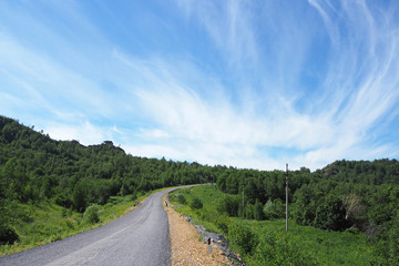 The landscape with the big asphalt road, the low green forest, the white clouds in the blue sky.