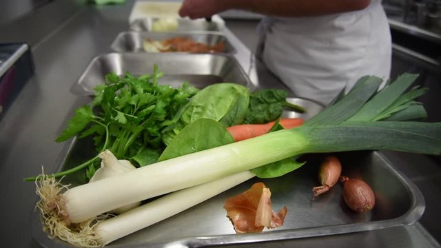 En cuisine professionnelles bac avec plusieurs l&eacute;gumes et une personne au fond qui &eacute;pluche