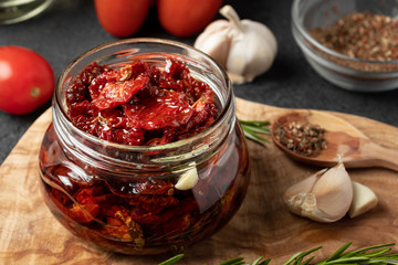 Sun-dried tomatoes with garlic, rosemary and spices in a glass jar on an olive wood cutting board