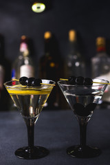 Dry martini with black olives and fresh lemon.Vermouth cocktail inside martini glass over dark background.Martini glasses are on the bar. selective focus