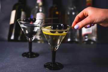 Dry martini with black olives and fresh lemon.Vermouth cocktail inside martini glass over dark background.Martini glasses are on the bar. selective focus