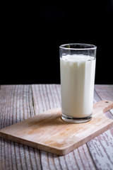 Glass of milk on wooden tray and black background. Healthy beverage concept.