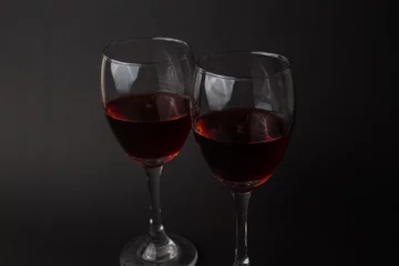 Fotobehang hermosas copas de vino transparentes con vino tinto sobre un fondo negro © Arvin