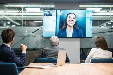 Employees listening to smiling leader during video conference. Business people looking at monitor screen during video conference in office. Business conference concept