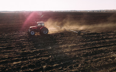 Farm tractor raising dust with harrow plow preparing land for sowing. Agriculture industry, cultivation of land.