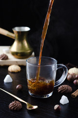 Hot coffee is poured into a transparent Cup from above. The hot steam coming from the mug