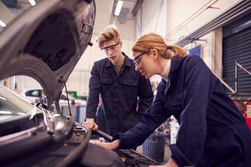 Male And Female Students Looking At Car Engine On Auto Mechanic Apprenticeship Course At College
