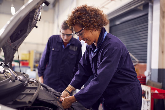 Female Tutor With Students Looking At Car Engine On Auto Mechanic Apprenticeship Course At College