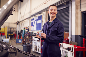 Male Motor Mechanic Wiping Hands After Working On Car Engine In Garage