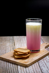 Square of cracker serve with fresh pink milk in glass on wooden tray with copy space for your text. Healthy beverage concept.