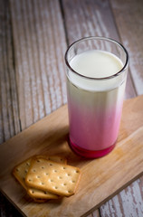 Fresh pink milk in glass serve with square of cracker on wooden tray with copy space for your text. Healthy beverage concept.