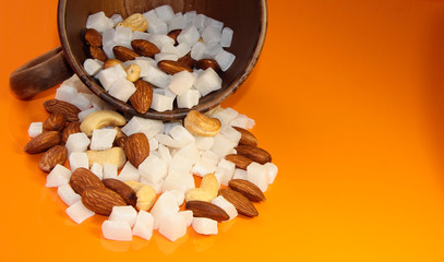 Cashew nuts, almonds and coconut in a mug on an orange background