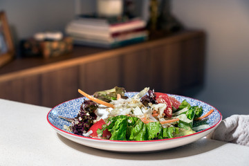 A salad plate with lettuce and tomatoes placed on a sofa over a home background.