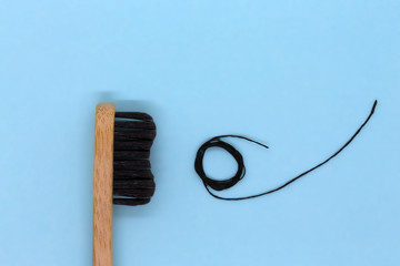 Black bamboo toothbrush and black dental floss on color blue background. Flat lay, close up