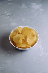 Salted spicy potato chips in a plate on a gray background top view
