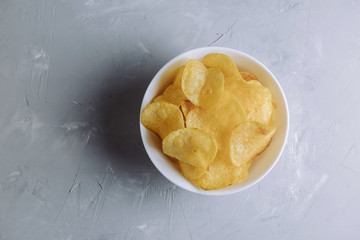 Salted spicy potato chips in a plate on a gray background top view