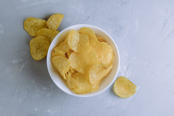 Salted spicy potato chips in a plate on a gray background top view