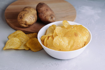 Salted chips in a plate with potatoes on a gray background side view