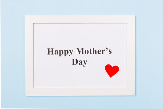 White picture frame with text Happy Mother's Day and red heart on light blue background . Happy Mother's Day concept.