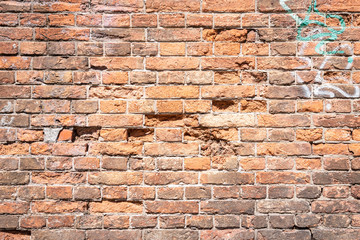 Eine alte verwitterte rotbraune Backsteinmauer mit Graffiti