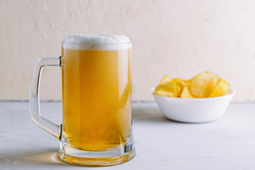Light beer in a large glass with froth and bubbles and potato chips side view