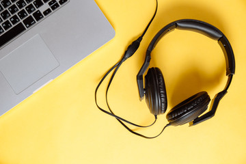 Laptop with stereo headphones on yellow background. Flat lay composition. Modern gadgets. Top view