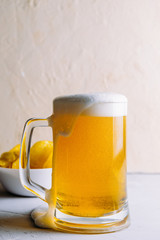 Light beer in a large glass with froth and bubbles and potato chips side view