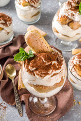Traditional italian dessert tiramisu. Many glasses with homemade tiramisu with chocolate cocoa powder, grey stone stone or concrete background.