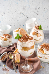 Traditional italian dessert tiramisu. Many glasses with homemade tiramisu with chocolate cocoa powder, grey stone stone or concrete background.