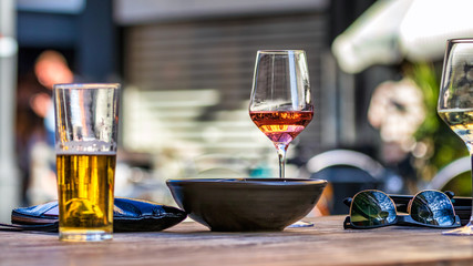 A red - rose wine glass placed on a wooden table next a bowl and other glasses, outdoors.