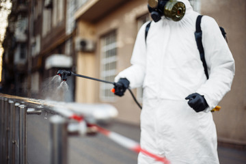 A man in protective equipment disinfects with a sprayer in the city. Surface treatment due to...