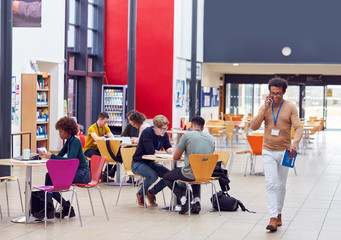 Communal Area Of Busy College Campus With Students Working At Tables And Tutor On Phone