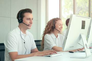Happy worker, staff with headphones working at call center service desk consultant smiling and laughing with colleagues, call centre service talking with the customer on hands-free phone