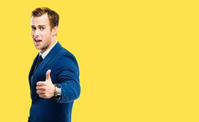 Excited businessman showing thumbs up like hand sign gesture, in blue confident suit, over yellow...